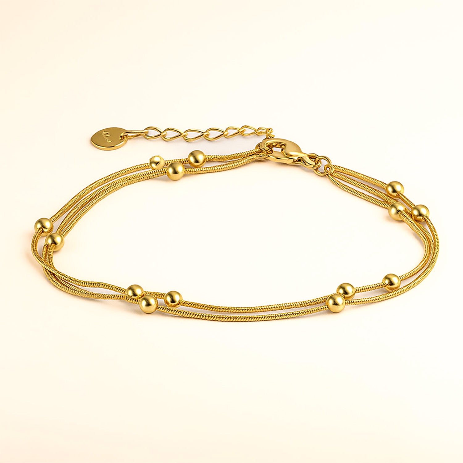 Gold bracelet with multiple chains and beads on a beige background